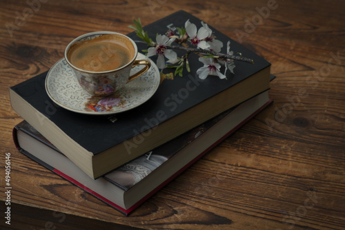 Cup of coffee on a old books and flowers on a wooden tablen. photo