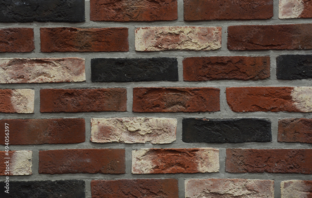 Fototapeta premium Clinker bricks background. A close-up of a clinker brick wall from dark red, white, orange and black bricks.