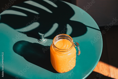 fresh orange juice in summer light and monstera or split-leaf philodendron leaves