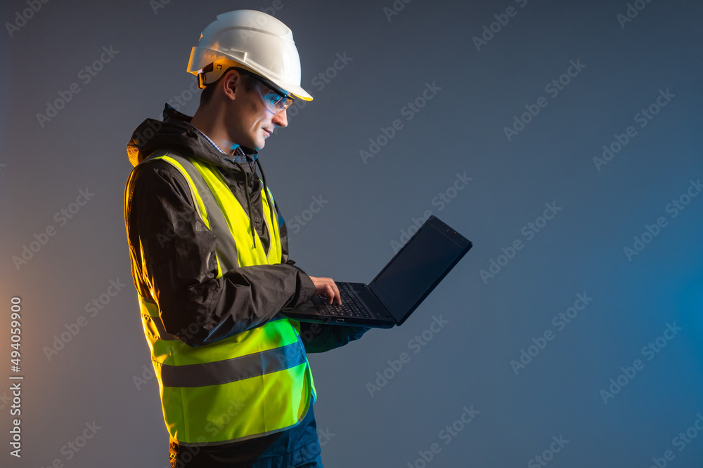 Computer engineer. Builder stands with laptop. Construction worker in yellow vest and helmet. Builders are working on laptop computer. Construction software concept. Technological engineer.
