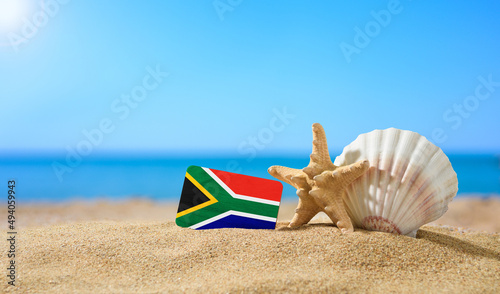 Tropical beach with seashells and South Africa flag. The concept of a paradise vacation on the beaches of South Africa.