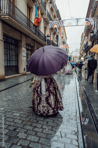 Fototapeta Naklejka Na Ścianę i Meble -  a fallera walks through the offering with an umbrella on a rain-soaked street