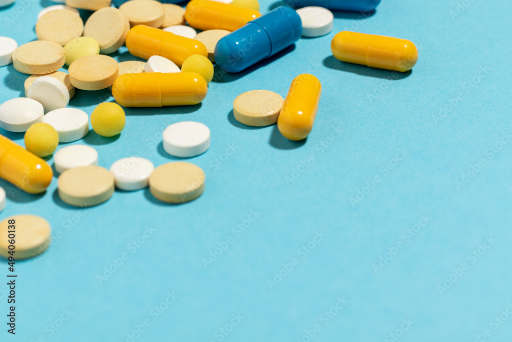 Different colored pills and capsules scattered on a blue background. With copy space.
