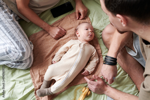 Принти на полотні Above view of cute baby boy in white romper grimacing while relaxing on bed betw