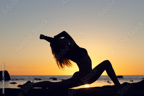 woman practicing stretching at sunset. seaside background  silhouette