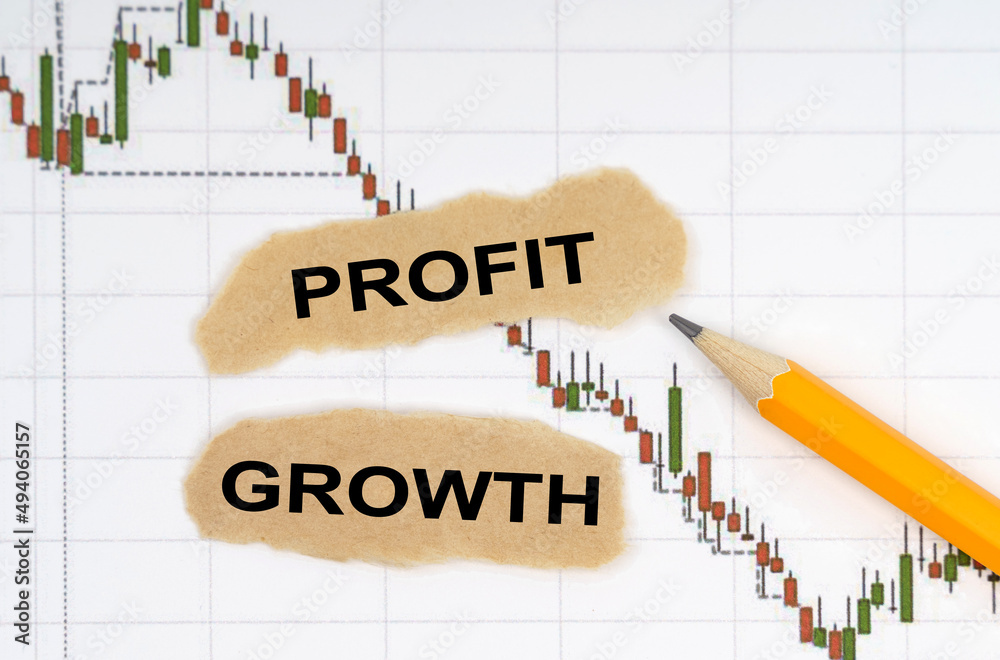 On the table with charts of quotes are a pencil and pieces of paper with the inscription - PROFIT GROWTH On the table with charts of quotes are a pencil and pieces of paper with the inscription - PROFIT GROWTH