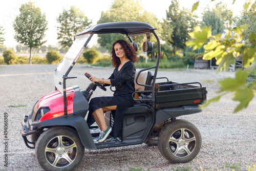 Beautiful, smiling, young brunette woman in black dress showing ok sign, posing in vehicle outside.