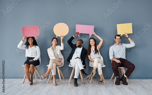 Let us deliver your good news. Portrait of a group of businesspeople holding speech bubbles while sitting in line against a grey background.