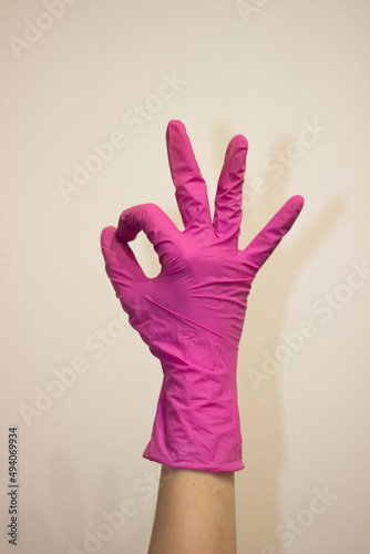 A woman s hand in a pink rubber glove shows the  OK  sign on a white background. The concept of protection. COVID-19. A hand in a pink rubber glove on a white background.