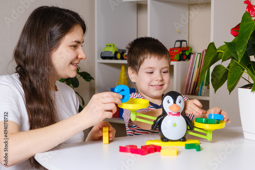 Mom and son play with numbers, weigh a penguin on a toy scale.