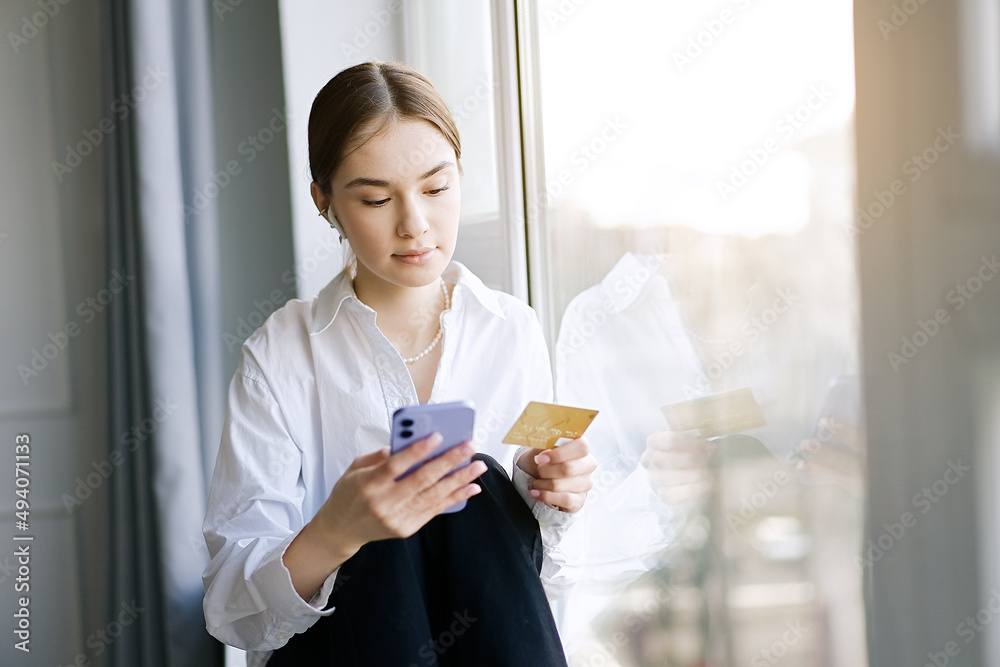Young woman using smartphone for shopping online with credit card at home in the living room Young woman using smartphone for shopping online with credit card at home in the living room