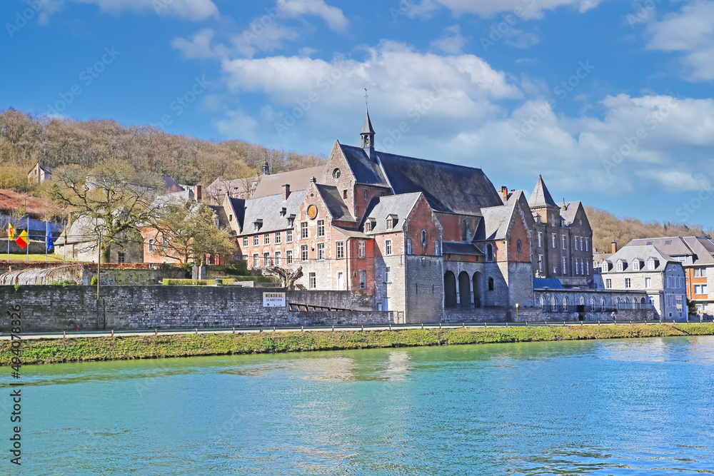 Dinant, Belgium - March 9. 2022: View over river meuse on medieval government building cpas aiginst blue sky, fluffy clouds