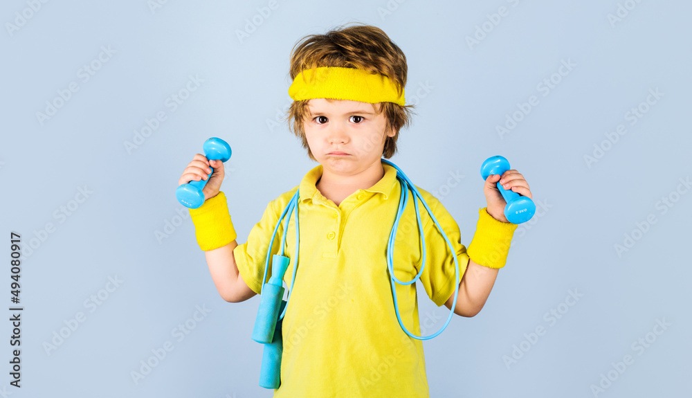 Child in sportswear with skipping rope and dumbbells. Sporty kid boy with jump rope and dumbbell.