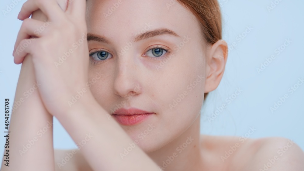 Young good-looking woman touches her skin sliding hand along a forearm, looks at camera and smiles