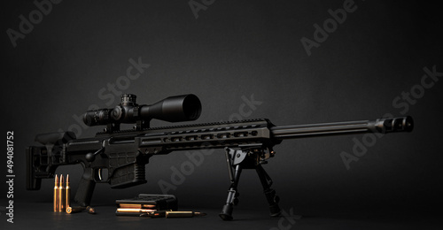 Modern powerful sniper rifle with a telescopic sight mounted on a bipod. Ammo and an additional magazine next to the rifle.