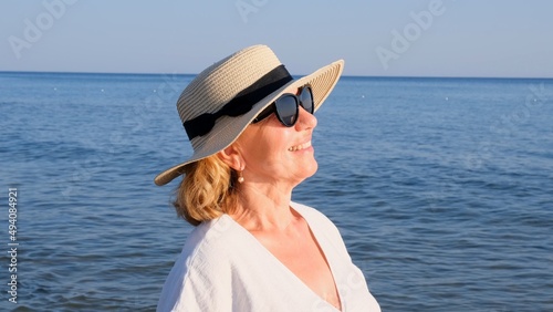 beautiful 50 year old woman in a straw hat and sunglasses on a blue sea background. Summer, vacation, vacation, active retirees