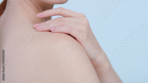 Close-up beauty portrait of young redhead woman softly touches her shoulder  turns and looks at camera against blue background