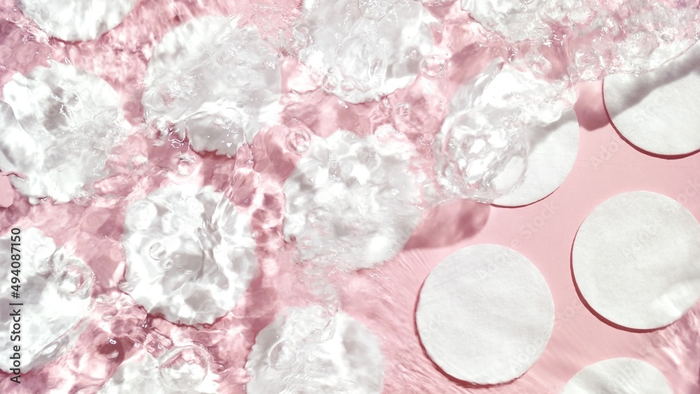 Cotton pads arranged in rows on pink background with water ripples over them | Background for beauty products Cotton pads arranged in rows on pink background with water ripples over them | Background for beauty products