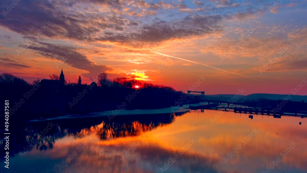 Incredible fiery sunrise sky reflected in calm river surface, with sea birds, moving aerial view.
