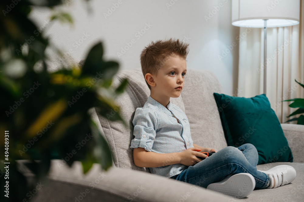 Happy boy playing video games holding game controller sitting on the coach in living room Happy boy playing video games holding game controller sitting on the coach in living room