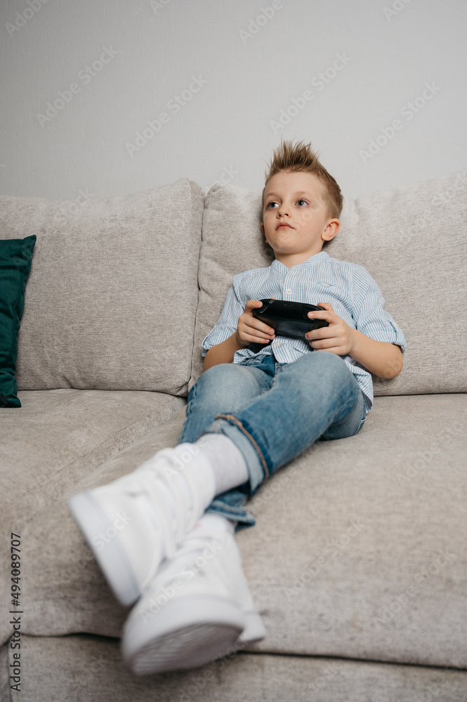 Happy boy playing video games holding game controller sitting on the coach in living room Happy boy playing video games holding game controller sitting on the coach in living room