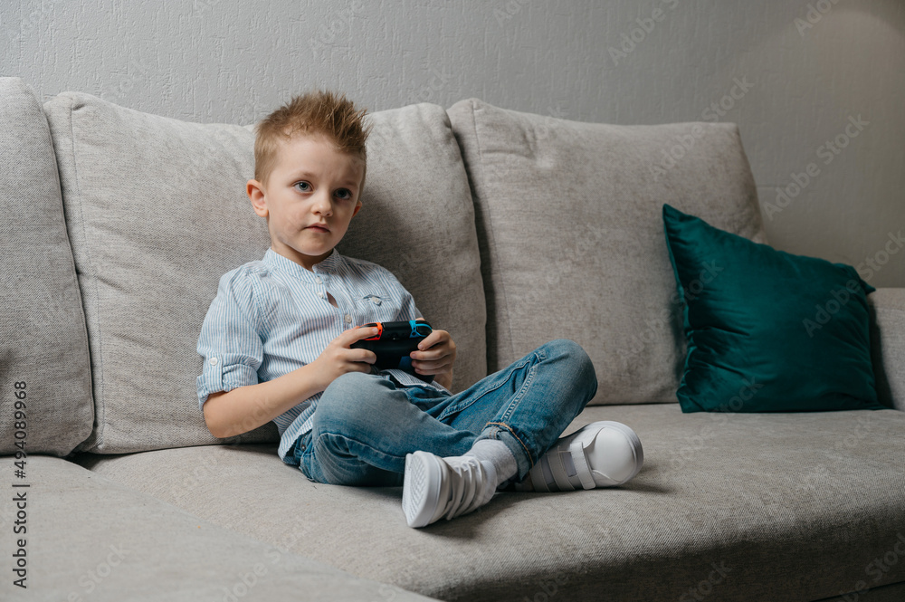 Happy boy playing video games holding game controller sitting on the coach in living room Happy boy playing video games holding game controller sitting on the coach in living room