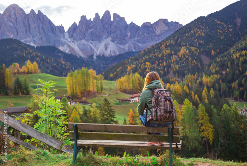 Girl with backpack on the bench with Dolomites mountains in background, Santa Maddalena village, Val di Funes valley, Trentino Alto Adige region, Italy, Europe