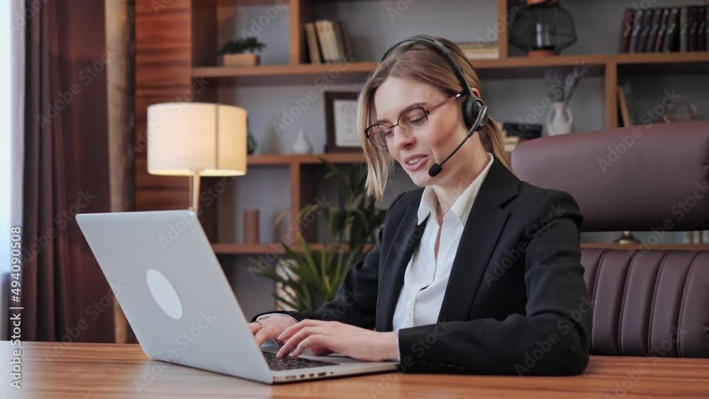 Millennial businesswoman sitting at home office desk wearing headset listens client via teleconferencing negotiating distantly, employee having lecture using laptop video call. Millennial businesswoman sitting at home office desk wearing headset listens client via teleconferencing negotiating distantly, employee having lecture using laptop video call.