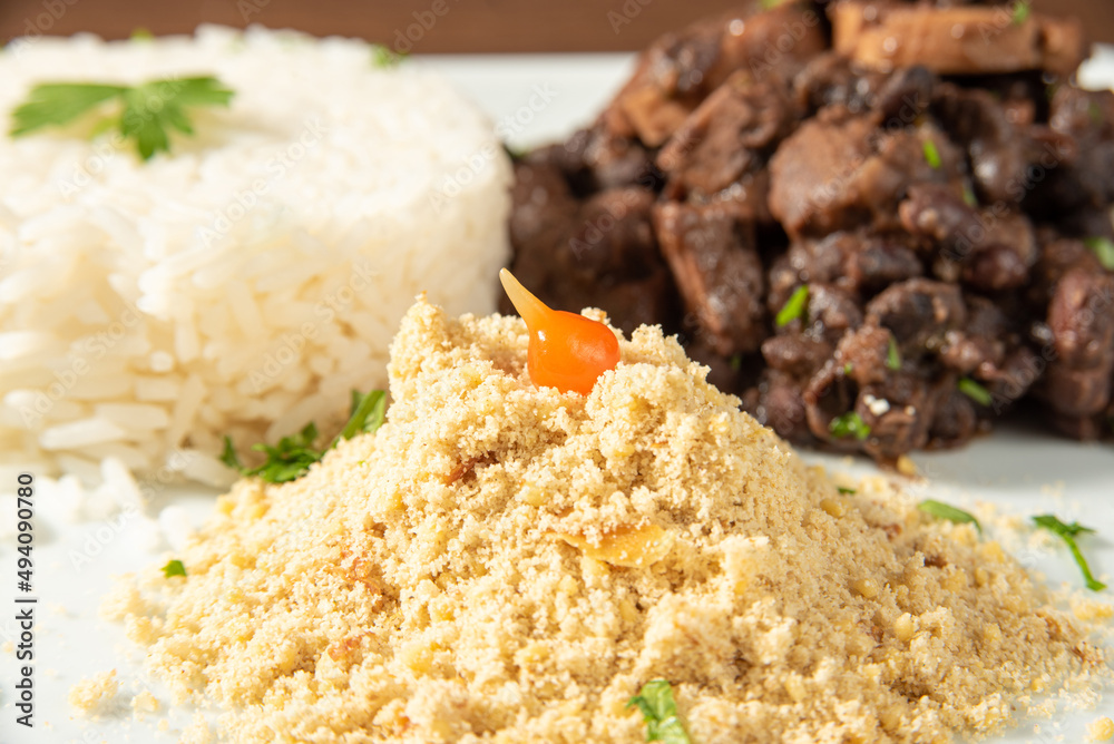 Vegan food, vegan feijoada, rice and farofa on a white plate, over wood, selective focus. Vegan food, vegan feijoada, rice and farofa on a white plate, over wood, selective focus.