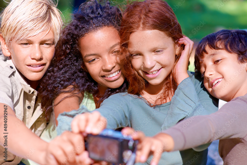 Fototapeta premium Capturing childhsummer moments. A group of kids looking at a digital camera while sitting outside.