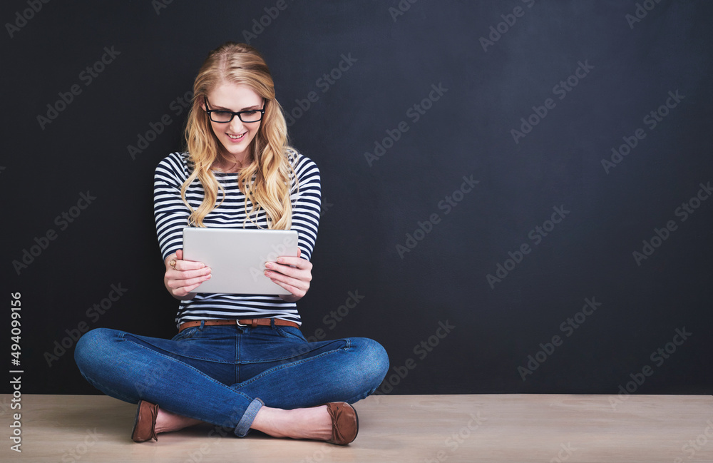Updating her social media. Studio shot of a young woman using a digital tablet against a dark background. Updating her social media. Studio shot of a young woman using a digital tablet against a dark background.