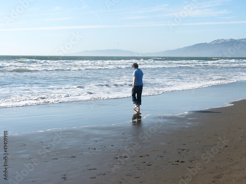 Woman in rolled jeans walking toward the surf on a bright beach day. photo