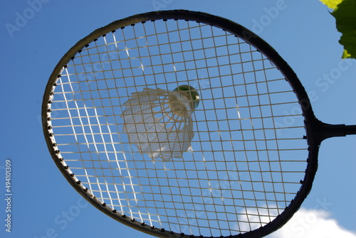 Playing badminton with racket and shuttlecock. A white plastic shuttlecock with a green stripe is visible through the white mesh with a square weave of a badminton racket. Sports Equipment. © Andrew_Swarga
