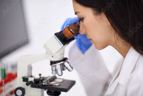 Shes a professional at blood-work. Profile of a female scientist viewing a sample through a microscope.
