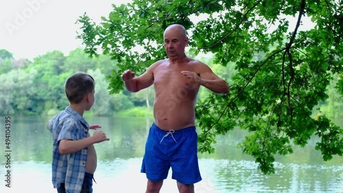 man, mature senior and child 8-10 years old do sports together by water on shore of a lake, concept of energy every day routine practice good man health mindfulness for strength and endurance photo