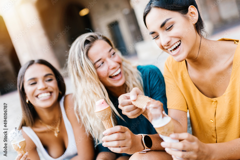 Happy multiethnic women laughing together outdoors - Diverse female friends having fun eating ice cream while sightseeing in an Italian city - Travel destination in Europe concept