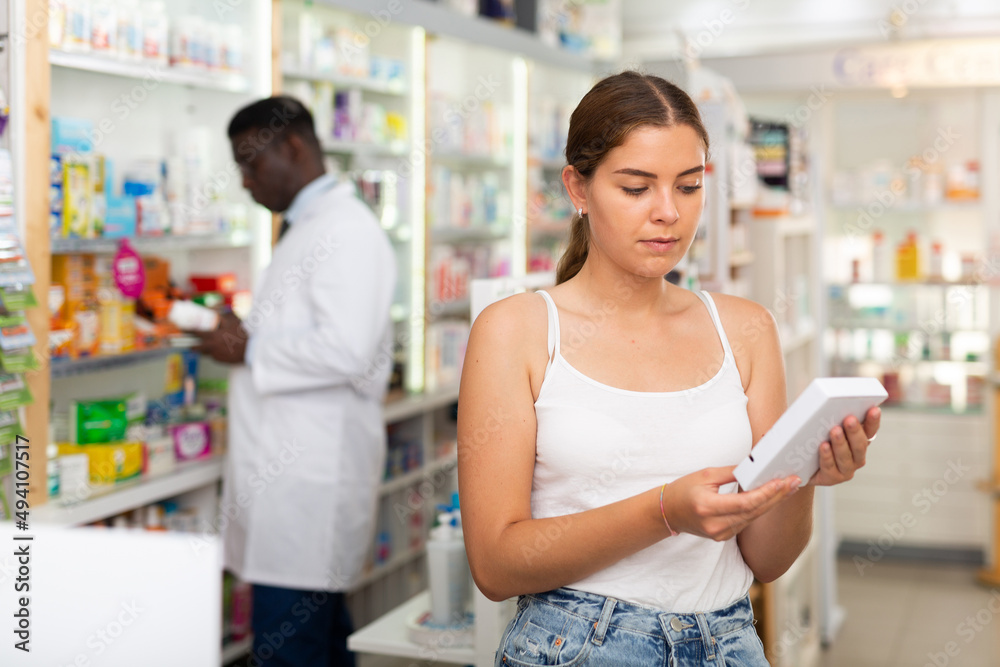 Brown-haired young lady choosing medicine in salesroom of drugstore