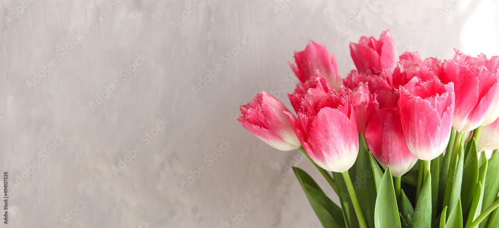 Banner with beautiful bouquet of pink tulips close-up against a gray wall with copy space. Flower arrangement. Springtime. Greeting card for the holidays. Selective focus Banner with beautiful bouquet of pink tulips close-up against a gray wall with copy space. Flower arrangement. Springtime. Greeting card for the holidays. Selective focus