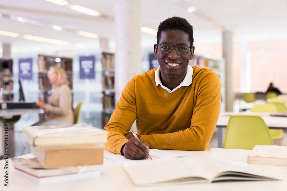 Obraz premium Portrait of happy african-american male student working with book in public library. High quality photo