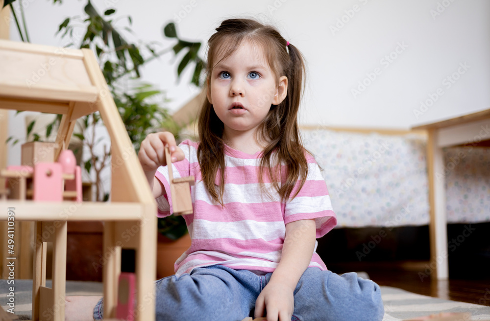 Montessori material. Child girl in pink T-shirt arranges wooden furniture in a doll house. Montessori material. Child girl in pink T-shirt arranges wooden furniture in a doll house.