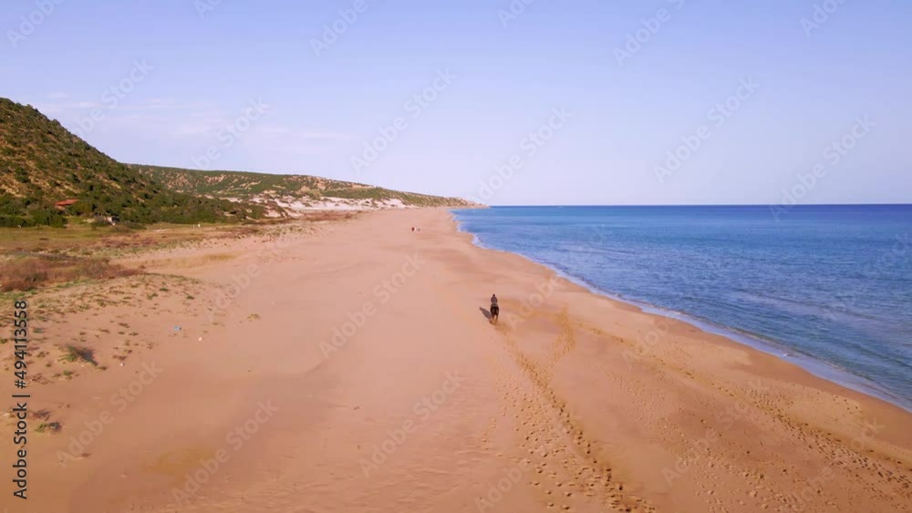 Aerial 4k man riding brown horse at natural sandy beach with crystal clear blue water and natural surrounding in Karpaz Peninsula, North Cyprus Aerial 4k man riding brown horse at natural sandy beach with crystal clear blue water and natural surrounding in Karpaz Peninsula, North Cyprus