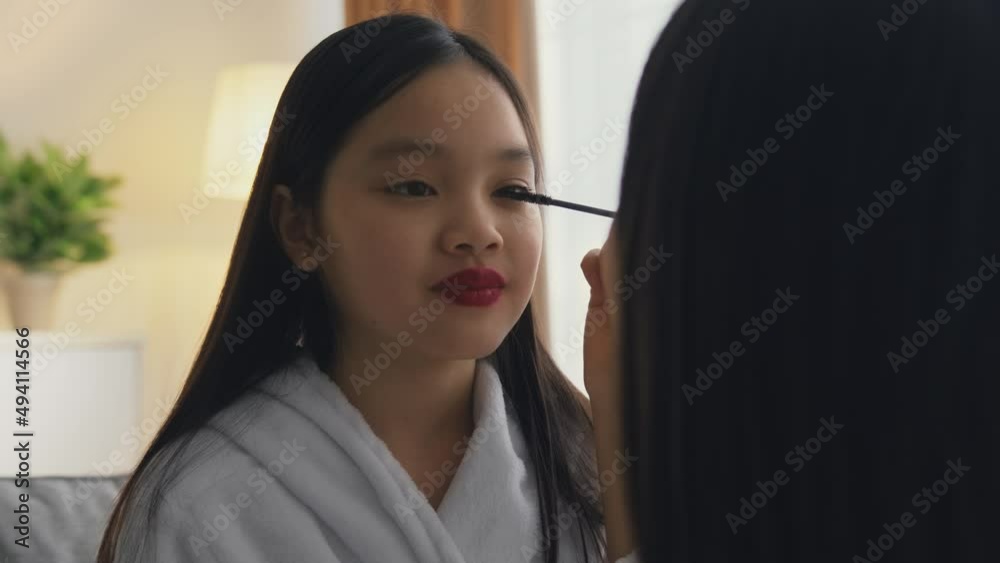 Feeling grown up. Loving mother making ceremonial make up to her little asian daughter, happy pretty girl smiling
