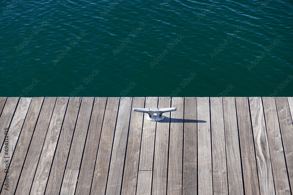 Obraz premium Wooden dock with mooring cleat, rippling blue-green waves in background, serenity, relaxation, vacation concept.