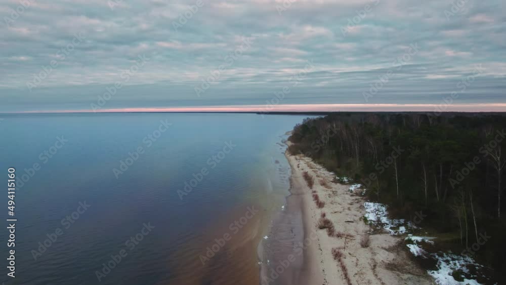 Drone flying over an old sandy beach with pine trees, the beach is small and very dirty. The sky is dark blue, almost sunset. the water is not clean, due to the fact that early spring Drone flying over an old sandy beach with pine trees, the beach is small and very dirty. The sky is dark blue, almost sunset. the water is not clean, due to the fact that early spring