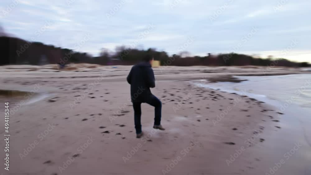 A cheerful and cheerful young guy in simple dark clothes dances on a sandy beach against the backdrop of pine trees and the sea, he dances calmly walking, relaxing, autumn and cold. paralax drone A cheerful and cheerful young guy in simple dark clothes dances on a sandy beach against the backdrop of pine trees and the sea, he dances calmly walking, relaxing, autumn and cold. paralax drone