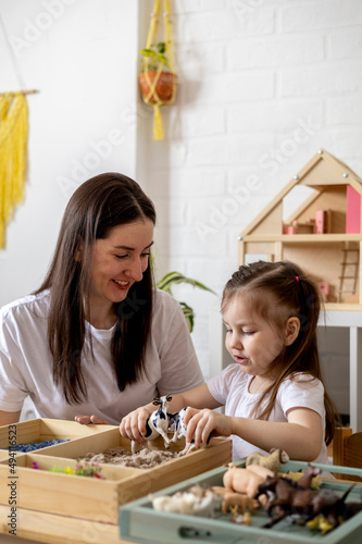 Montessori material. Little girl with her mom explores the farm animals in the game. Sensory box.