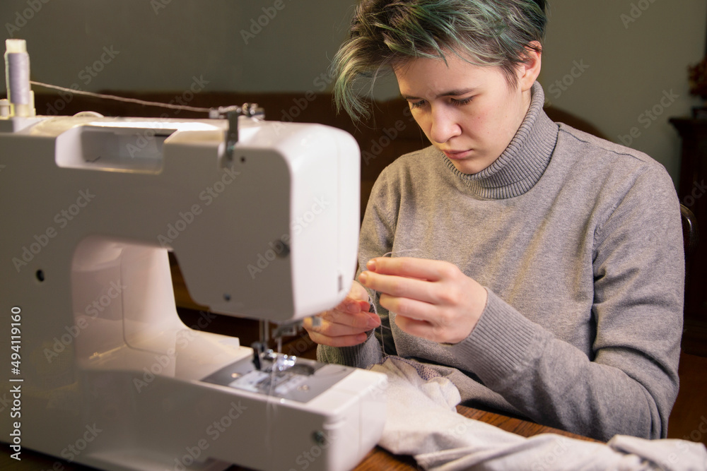 The girl sews while sitting at the sewing machine. Skill, hobby, profession.