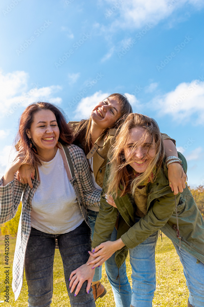 Three diverse girlfriends are having fun and hugging. Blue sky background.