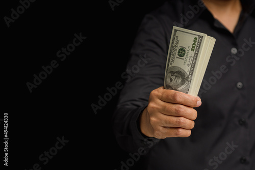 Hand of a businessman in a black shirt holding US dollars banknote while sitting in the office