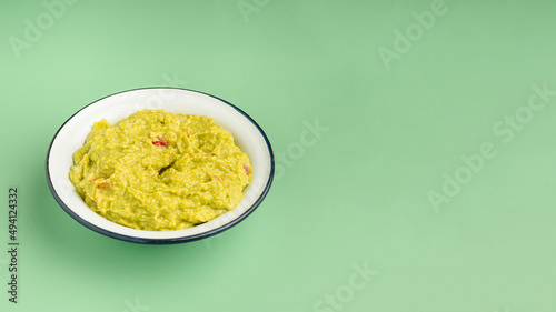 Fresh guacamole in a bowl over a green background
